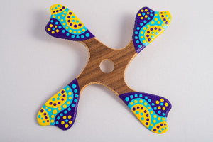 Boomerang quadripale Balabalaa en bois motifs pointillistes jaune violet et turquoise sur fond blanc