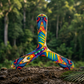 Colorful three-blade boomerang with butterfly-inspired printed design, displayed outdoors in a tropical forest setting