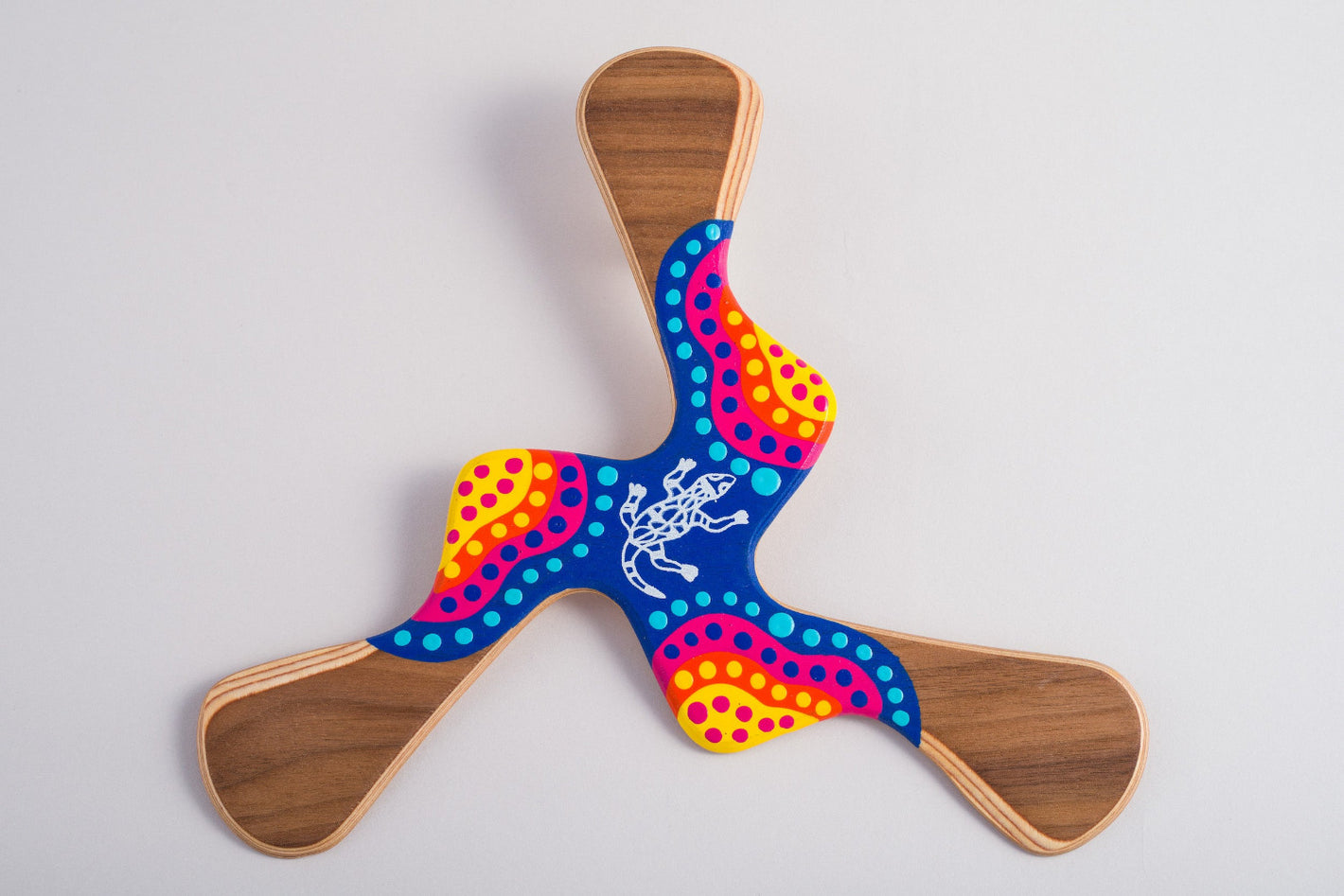 Boomerang Kadina 3 ailes avec lézard aborigène central et décoration pointilliste multicolore jaune orange rose et bleu, coucher de soleil australien