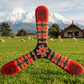     Three-blade Maori boomerang with red and black tribal patterns, posed on a New Zealand green meadow with snowy mountains