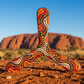     Three-blade Ozzie boomerang with Aboriginal dot art in red, orange and black, standing in the Australian outback near Uluru

