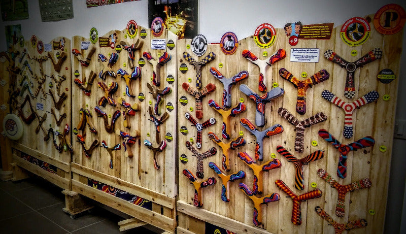 Présentoir en bois exposant une large collection de boomerangs colorés bipale et tripale dans une boutique 