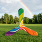 Colorful three-blade boomerang with rainbow swirl pattern, posed on green grass with a rainbow in the sky