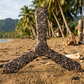 Three-wings Samoa boomerang with black Polynesian tattoo patterns, on a tropical sandy beach with palm trees and tiki statues