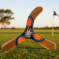 Boomerang Warramba tripale en bois, motif tortue aborigène, pointillés rouge orange turquoise, terrain australien