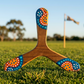 Boomerang tripale Warukay en bois motifs pointillistes orange et bleu sur herbe