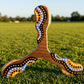 Boomerang tripale Wata en bois motifs pointillistes orange et blanc sur herbe