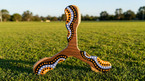 Boomerang tripale Wata en bois motifs pointillistes orange et blanc sur herbe
