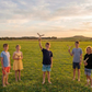 Cinq enfants tenant des boomerangs en bois dans un champ au coucher de soleil, atelier boomerang pour enfants en plein air