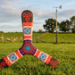 Boomerang tripale Celtic aux motifs triskel et entrelacs celtiques rouge, violet et turquoise, posé dans un pré irlandais verdoyant