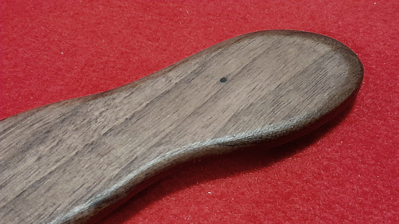 Détail de la poignée en bois de noyer d'un bâton de jet gaulois – texture naturelle sur fond rouge 