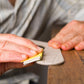 Artisan ponçant à la main un boomerang en bois brut avec du papier de verre