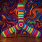 Boomerang tripale Seventies aux rayures arc-en-ciel, posé devant un fond psychédélique tourbillonnant et champignons colorés